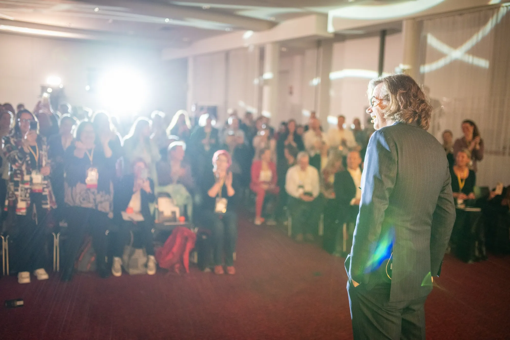 Speaker auf Bühne vor Publikum bei Business-Event mit Applaus und heller Beleuchtung